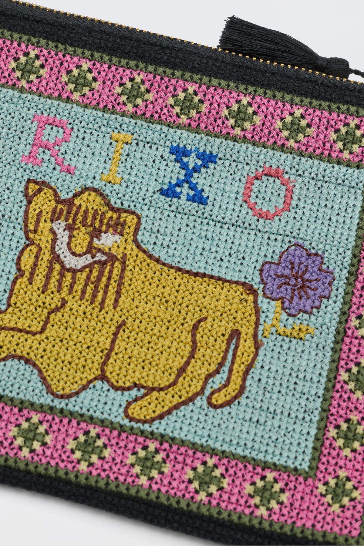 A close-up of the Beau - Mini Leo Cross Stitch Embroidery Charcoal pouch, showcasing a yellow lion, purple flower, and multicolored "RIXO" lettering bordered by a vibrant pink and green floral pattern.