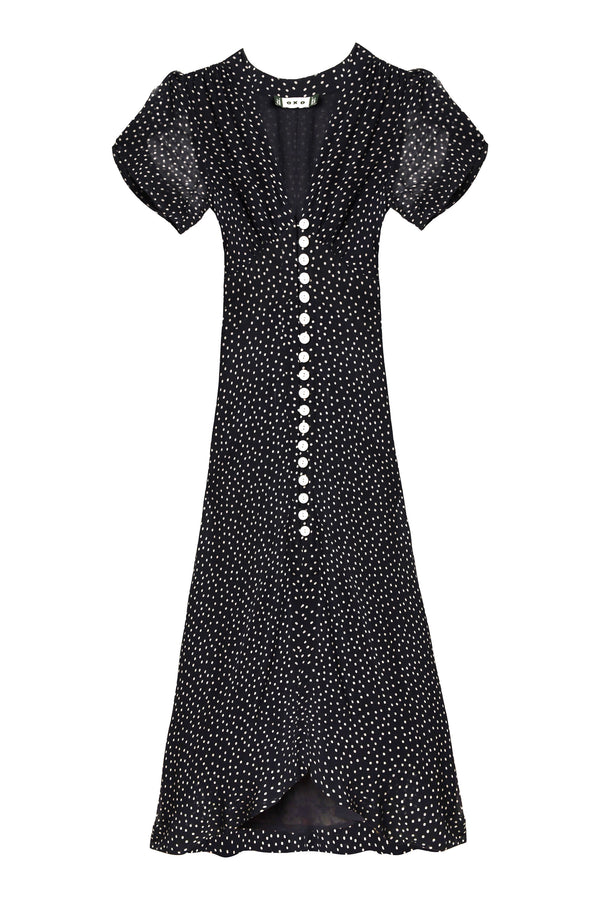The Novara - Painted Spot Deep Navy dress features a classic polka-dot print, short sleeves, a V-neck, white front buttons, a fitted waist, and a slightly flared hem.