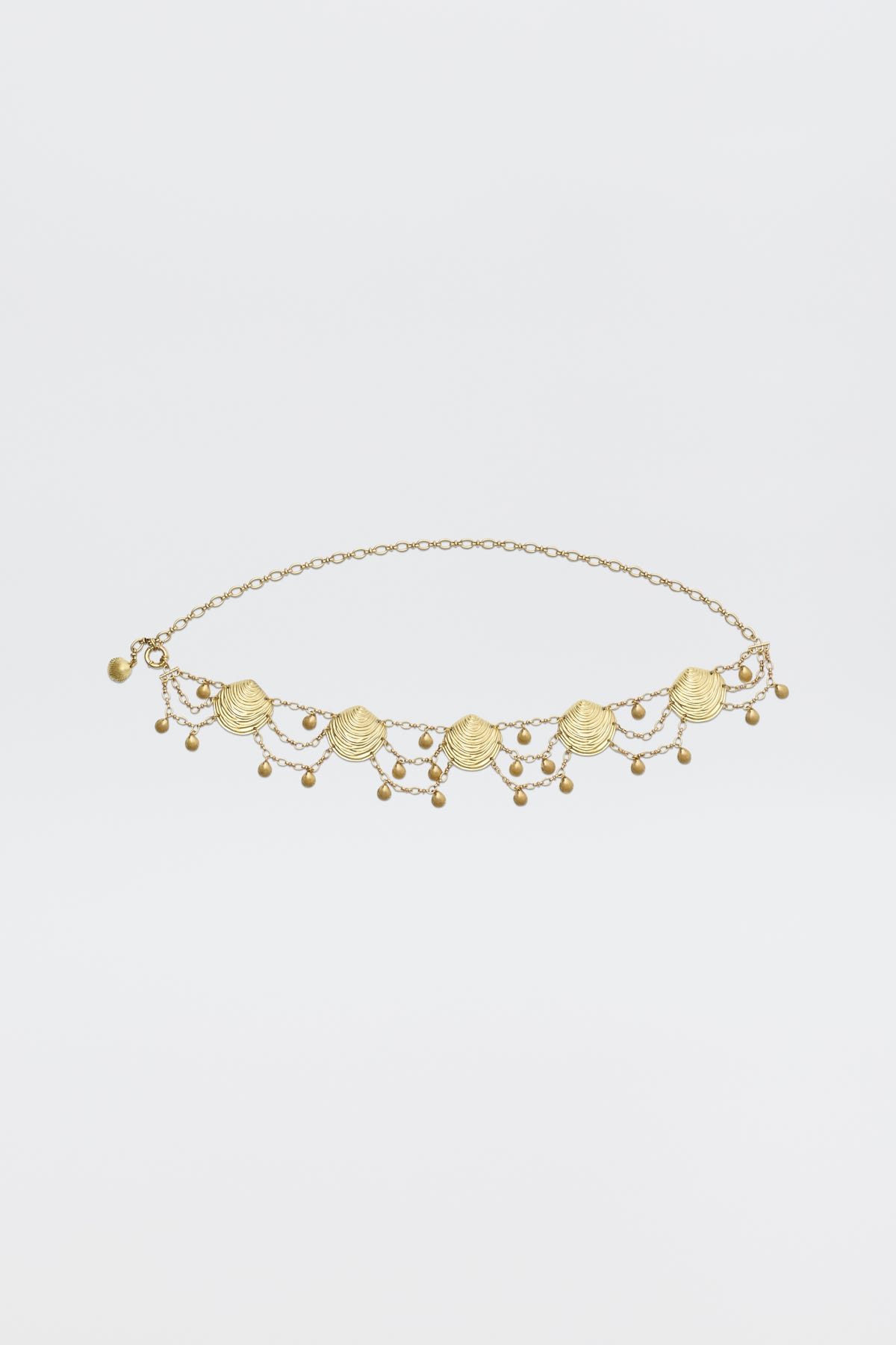 The Asia - Gold necklace is a delicate gold piece with small scallop shell charms and dangling beads symmetrically arranged on a fine chain, shown against a plain white background.