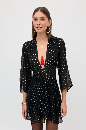 A woman wearing a Clove - Gold Spot Black long-sleeved mini dress, gold jewelry, and a red tassel necklace.