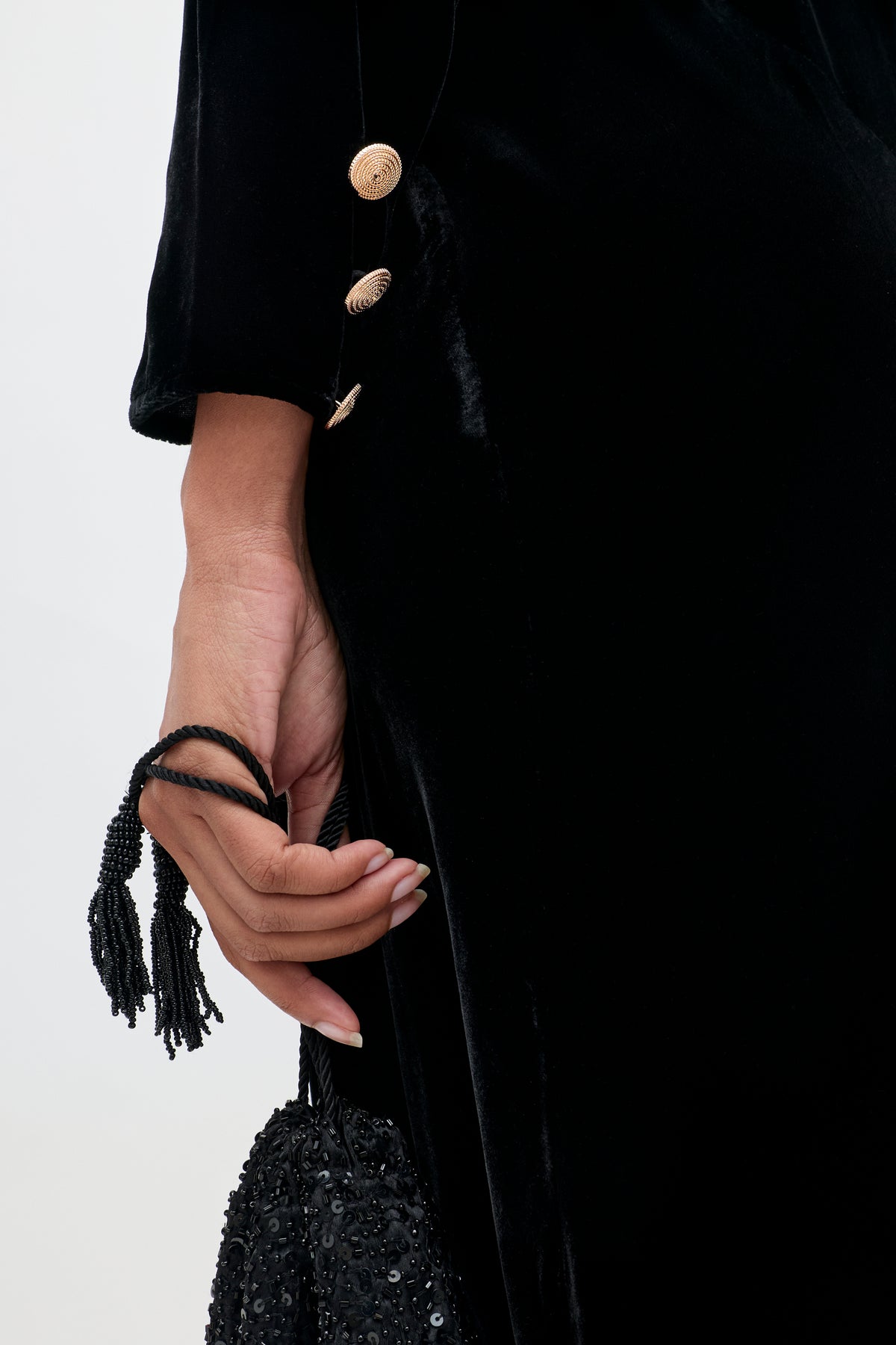 A hand holding the Devina - Black beaded purse with tassels, styled with a black velvet gown featuring gold sleeve buttons.