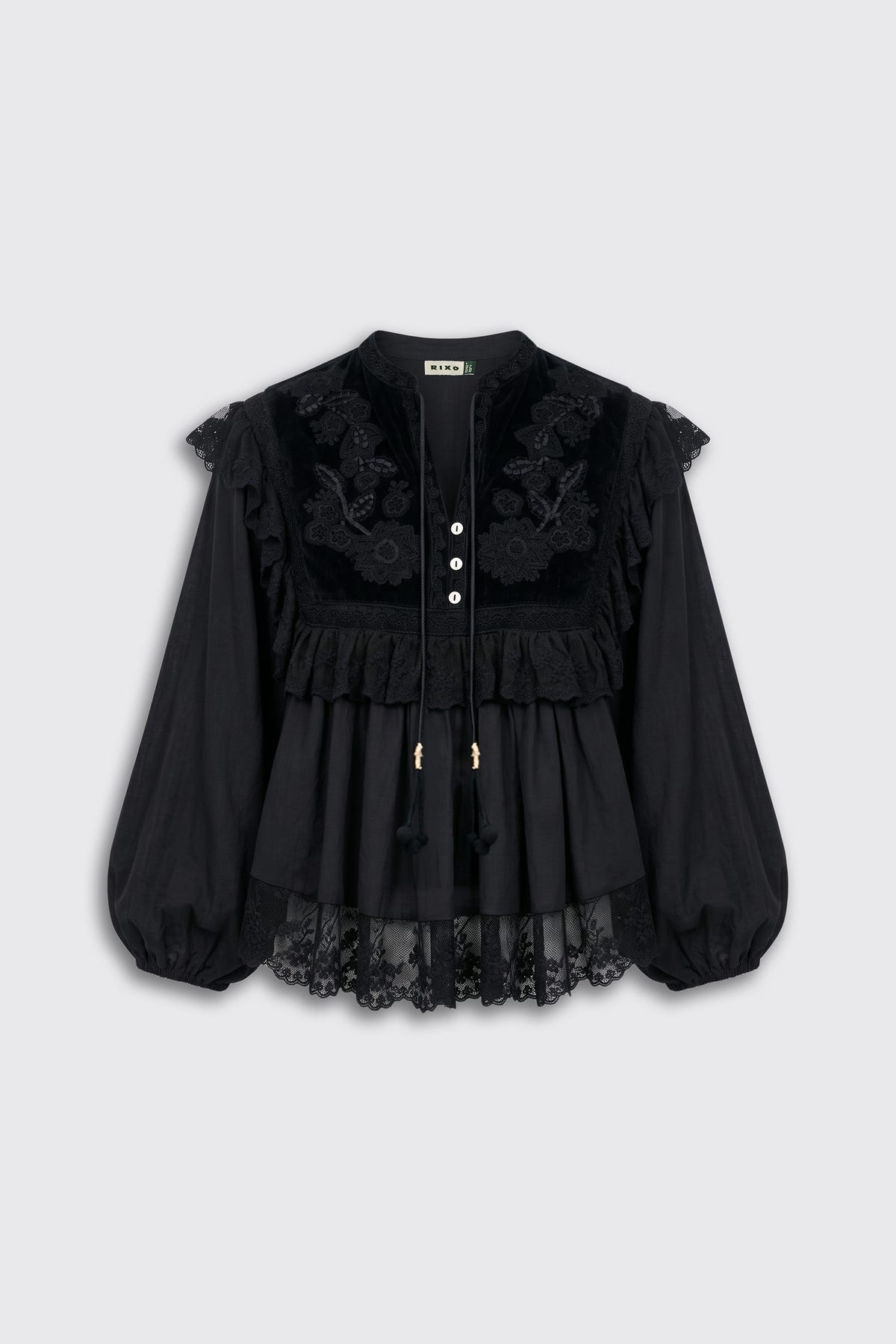 Diann - Lilly Embroidery Black is a black long-sleeve blouse featuring lace detailing, floral embroidery, ruffles, and a row of white buttons down the front. Designed for a loose fit, it has sheer lace edging at the sleeves and hem.