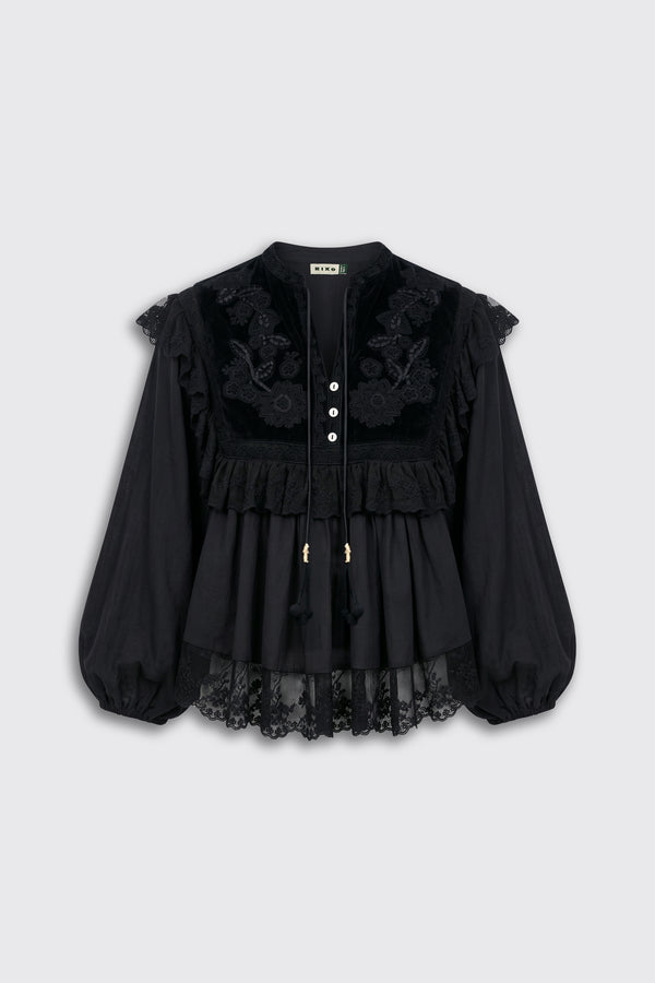 Diann - Lilly Embroidery Black is a black long-sleeve blouse featuring lace detailing, floral embroidery, ruffles, and a row of white buttons down the front. Designed for a loose fit, it has sheer lace edging at the sleeves and hem.