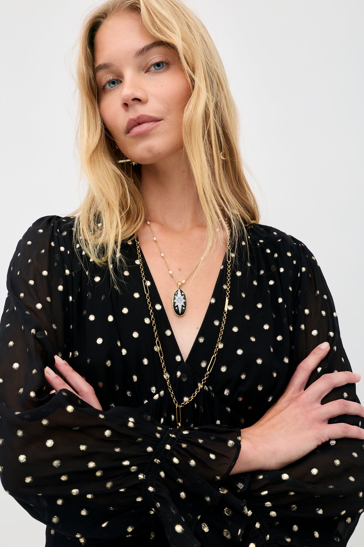 A person wearing the Ethel - Gold Spot Black long-sleeved dress with a metallic gold polka dot pattern and a pendant necklace.