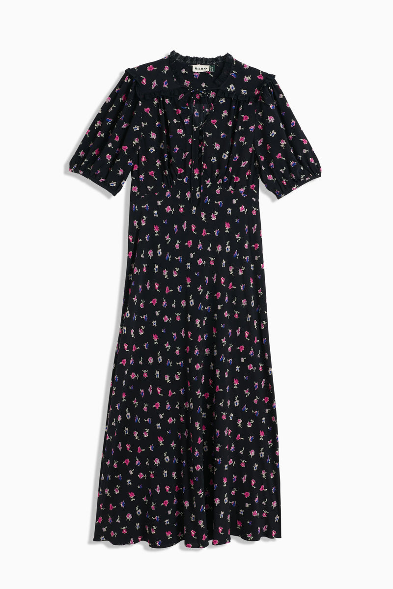 The Gwen - French Ditsy Black dress is a black midi with short sleeves, pink, white, and purple floral prints, a ruffled high neckline with tie detail—ideal for easy day-to-night wear.
