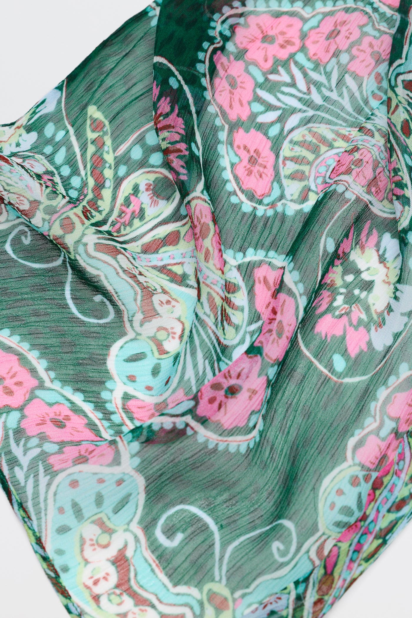 The "Julien - Butterfly Bloom Green" scarf features a sheer green fabric adorned with vibrant pink, blue, and white floral and butterfly patterns, draped gracefully in soft folds.