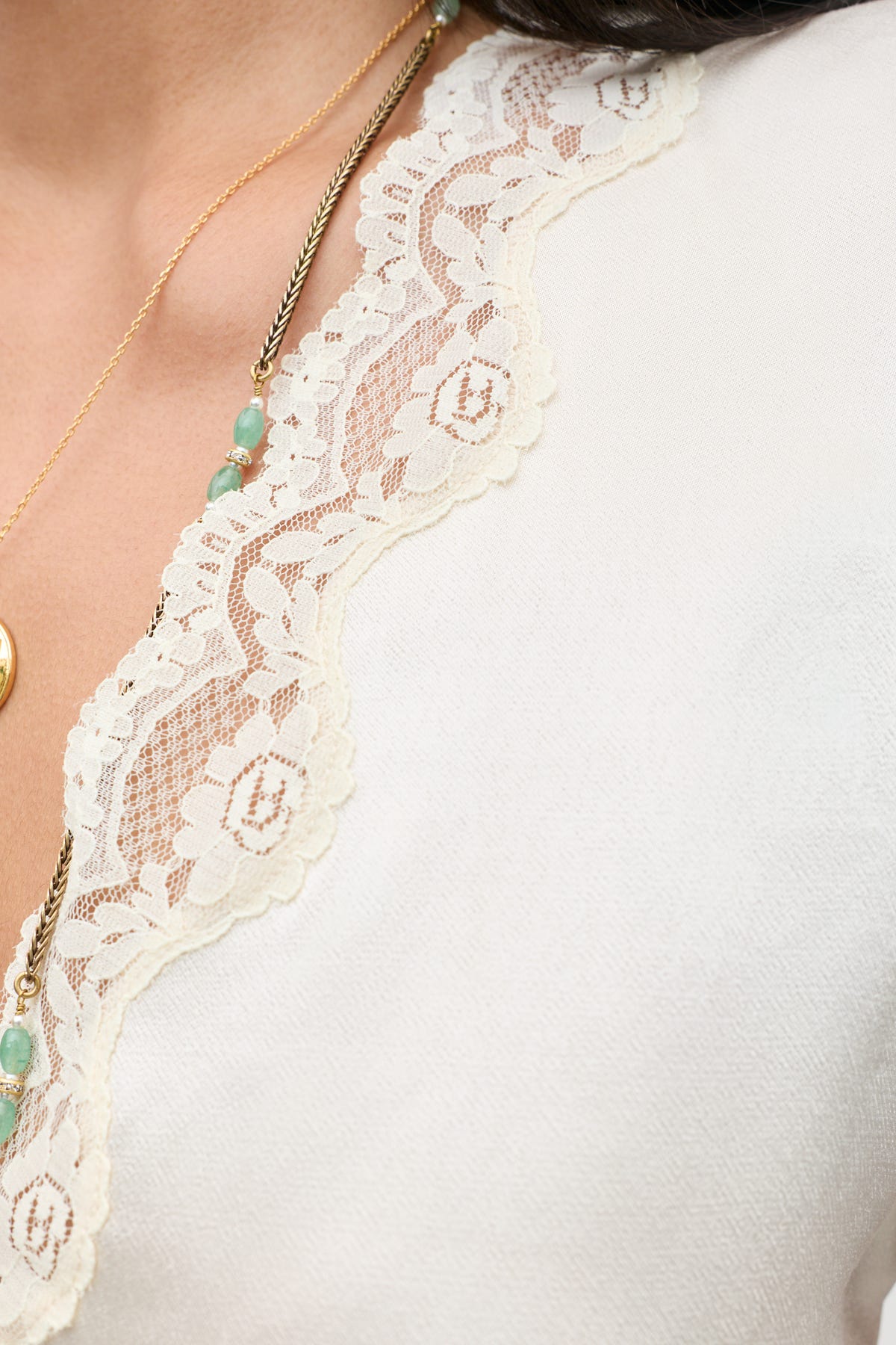 Close-up of a woman’s neckline wearing the Karia - Champagne top featuring a scalloped lace trim, styled with layered gold necklaces adorned with turquoise beads.
