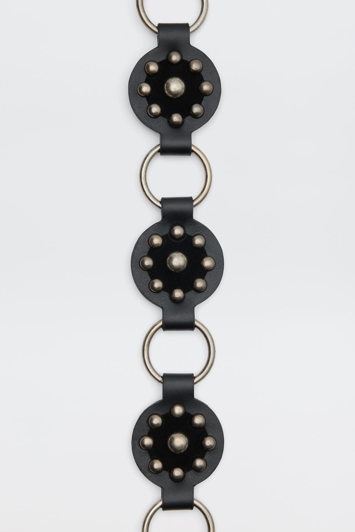 Kassy - Black: A vertical black leather strap featuring circular metal-studded accents connected by large silver rings, shown against a plain white background.