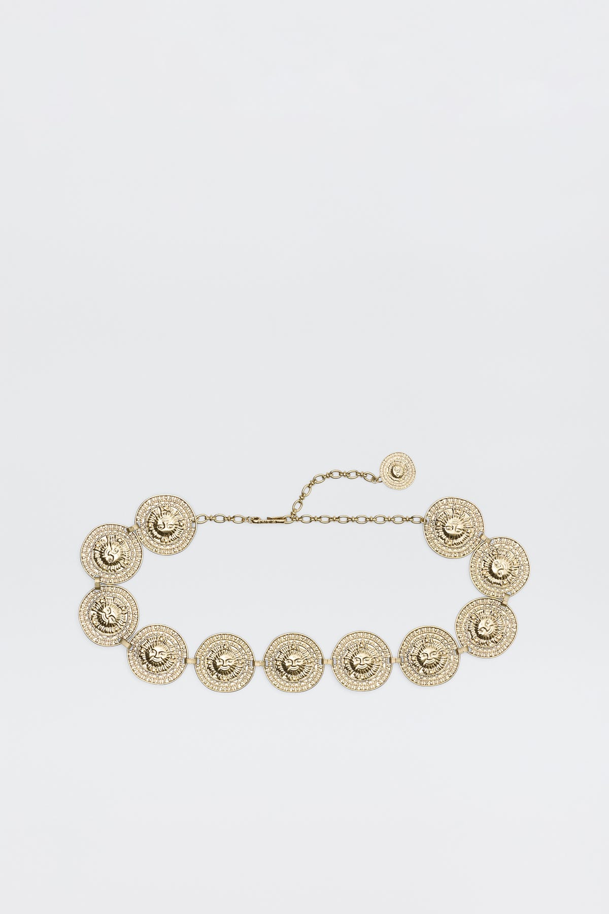 Leyla - Gold is a gold chain belt with round, ornate medallions linked together, each featuring intricate textured detailing and an adjustable chain clasp, shown on a plain white background.