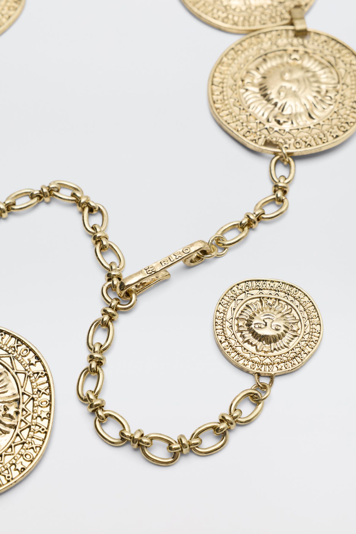 Close-up of the Leyla - Gold necklace, showcasing large round textured medallions with intricate designs and a decorative clasp, displayed on a light gray background.