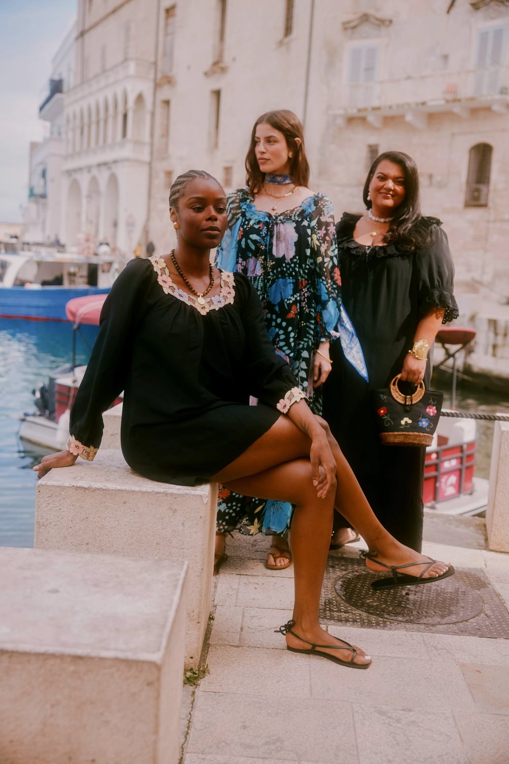 Three women posing together by a waterfront with a scenic background