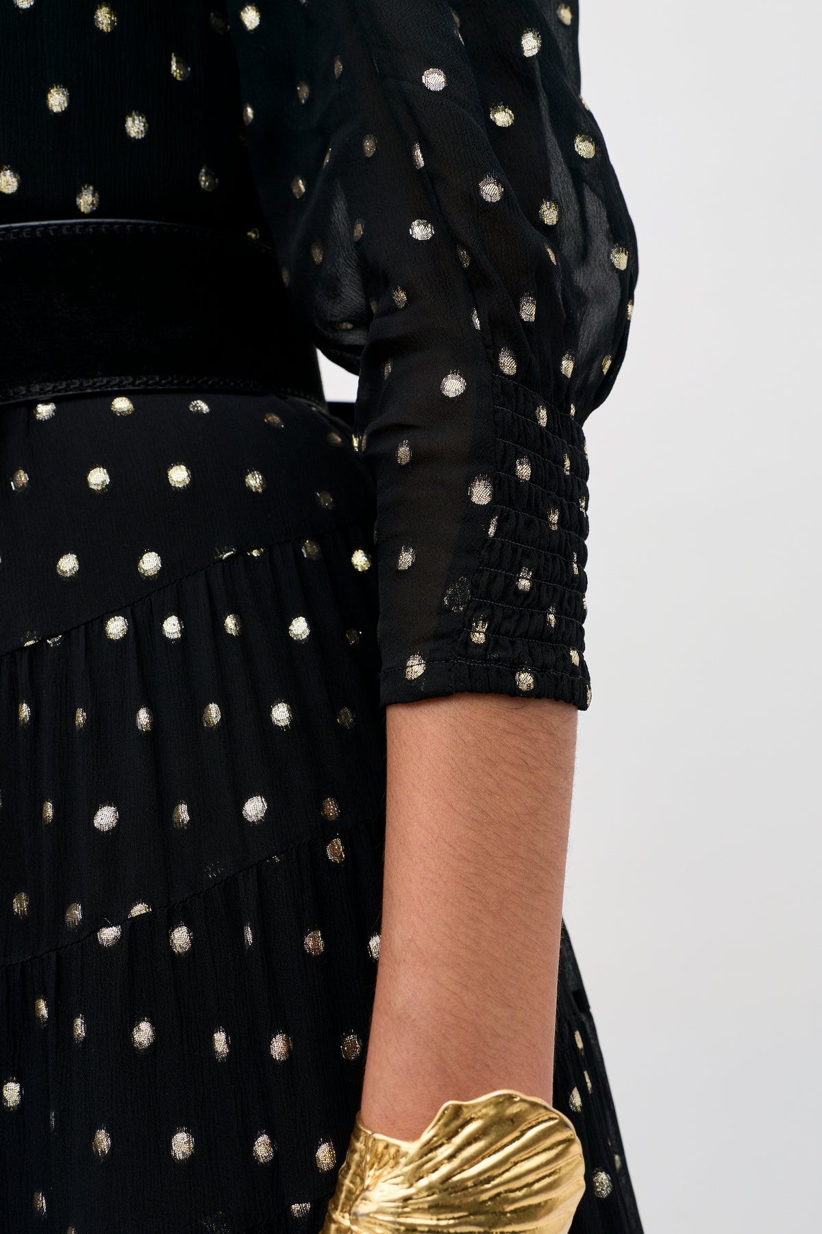 Lucina - Gold Spot Black dress featuring gold polka dots, shirred three-quarter sleeves, and a gold cuff bracelet.