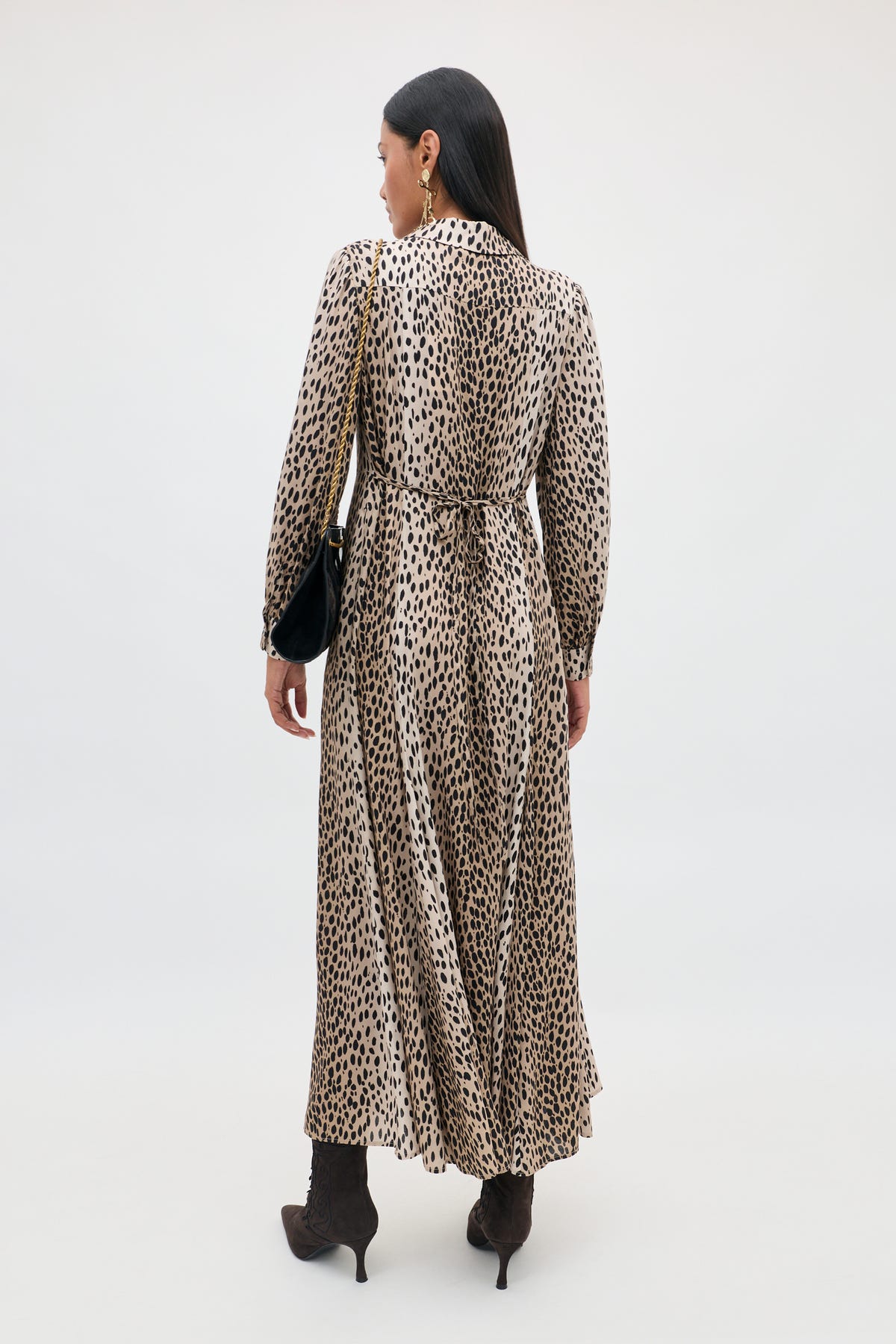A petite woman with long dark hair, seen from behind, showcases effortless everyday style in the Maddison - Antelope Spot Black long-sleeved, ankle-length shirt dress, paired with black boots and a black shoulder bag against a plain light background.