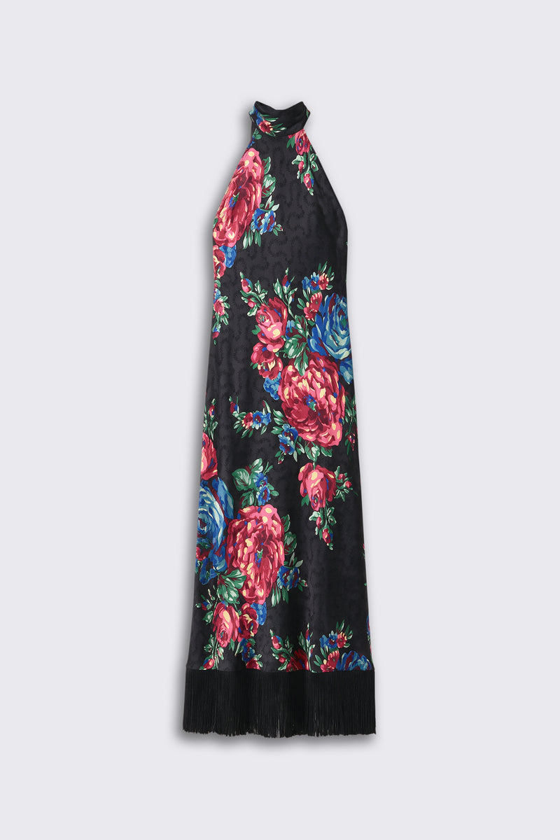 The “Maura - Vintage Bouquet Black” dress features a black halter-neck design adorned with a bold floral pattern in shades of red, pink, blue, and green, finished with a black fringe trim along the bottom hem. The dress is displayed against a plain light background.