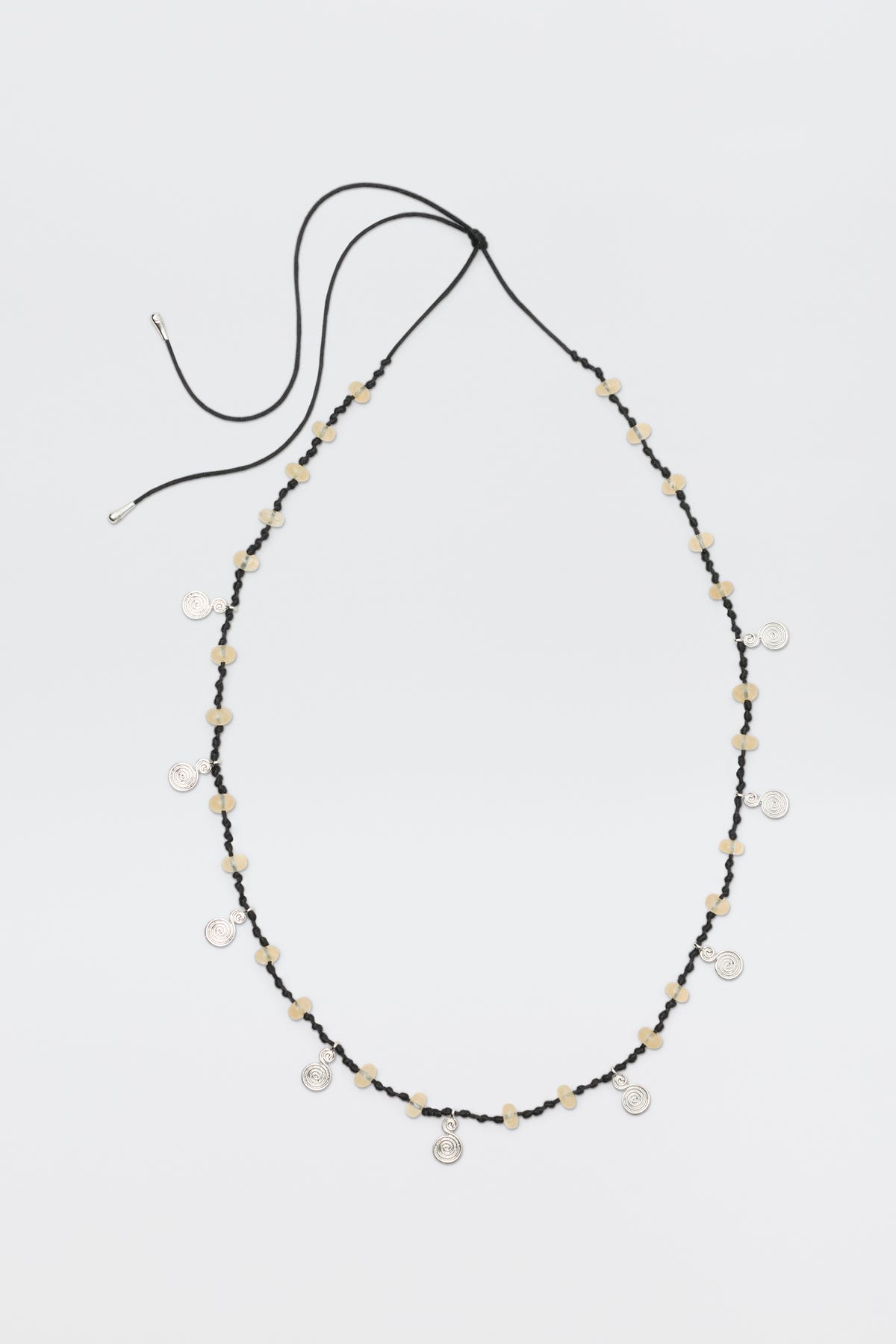 A long black cord necklace called "Mikah - Silver," featuring beige beads and small round silver charms evenly spaced, is displayed on a plain white background with the cord ends untied.