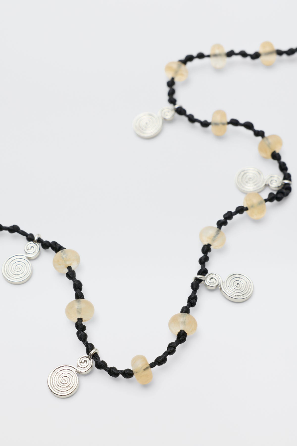 Mikah - Silver: A black knotted necklace featuring round translucent yellow beads and spiral silver charms spaced along its length, displayed on a white background.