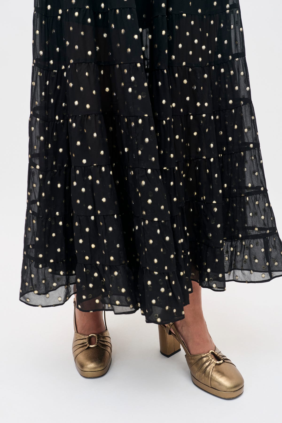 Moreen - Dark Gold black tiered skirt with gold polka dots worn with metallic gold block-heeled pumps.