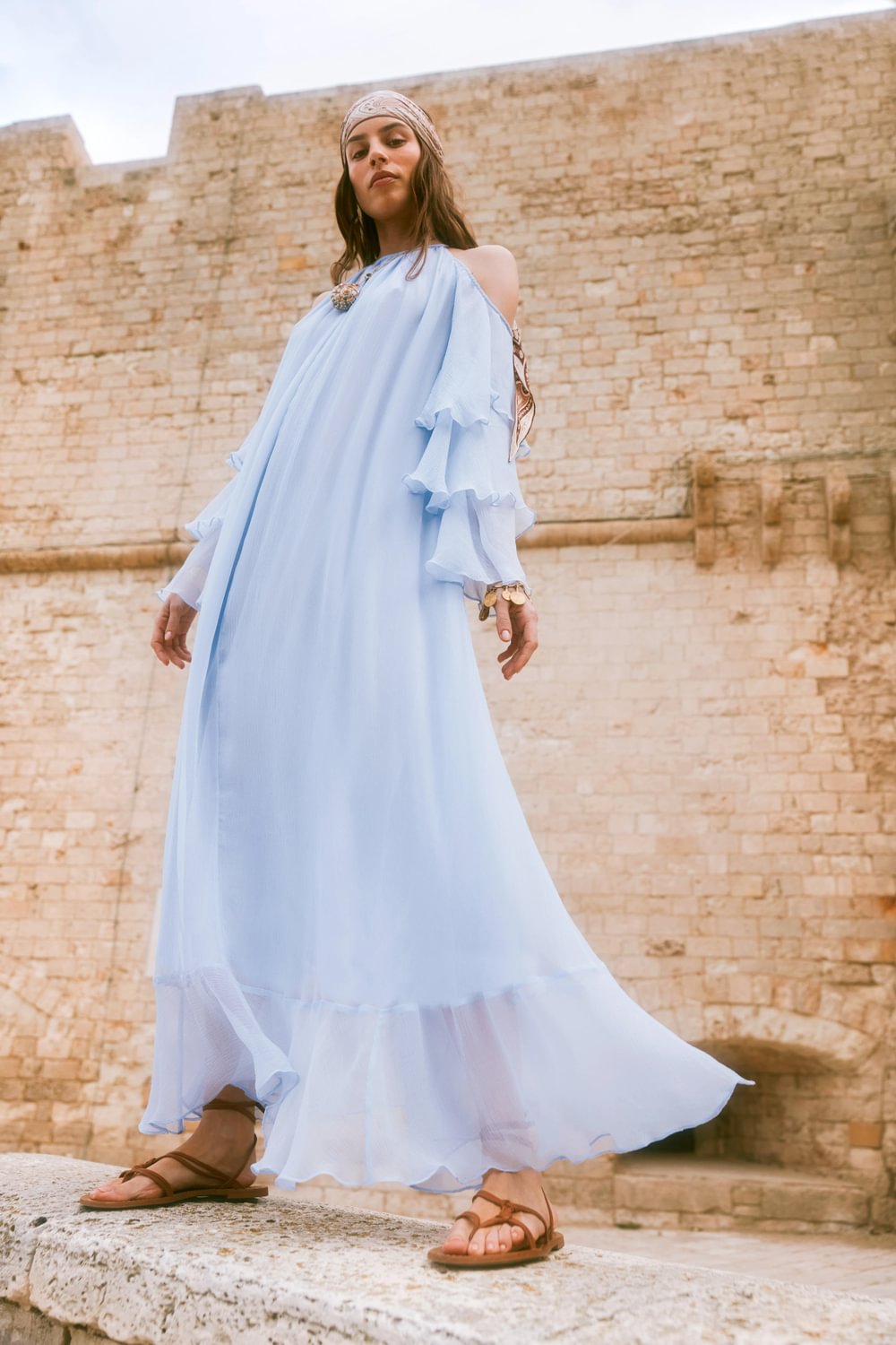 Woman in a light blue dress standing against a stone wall.