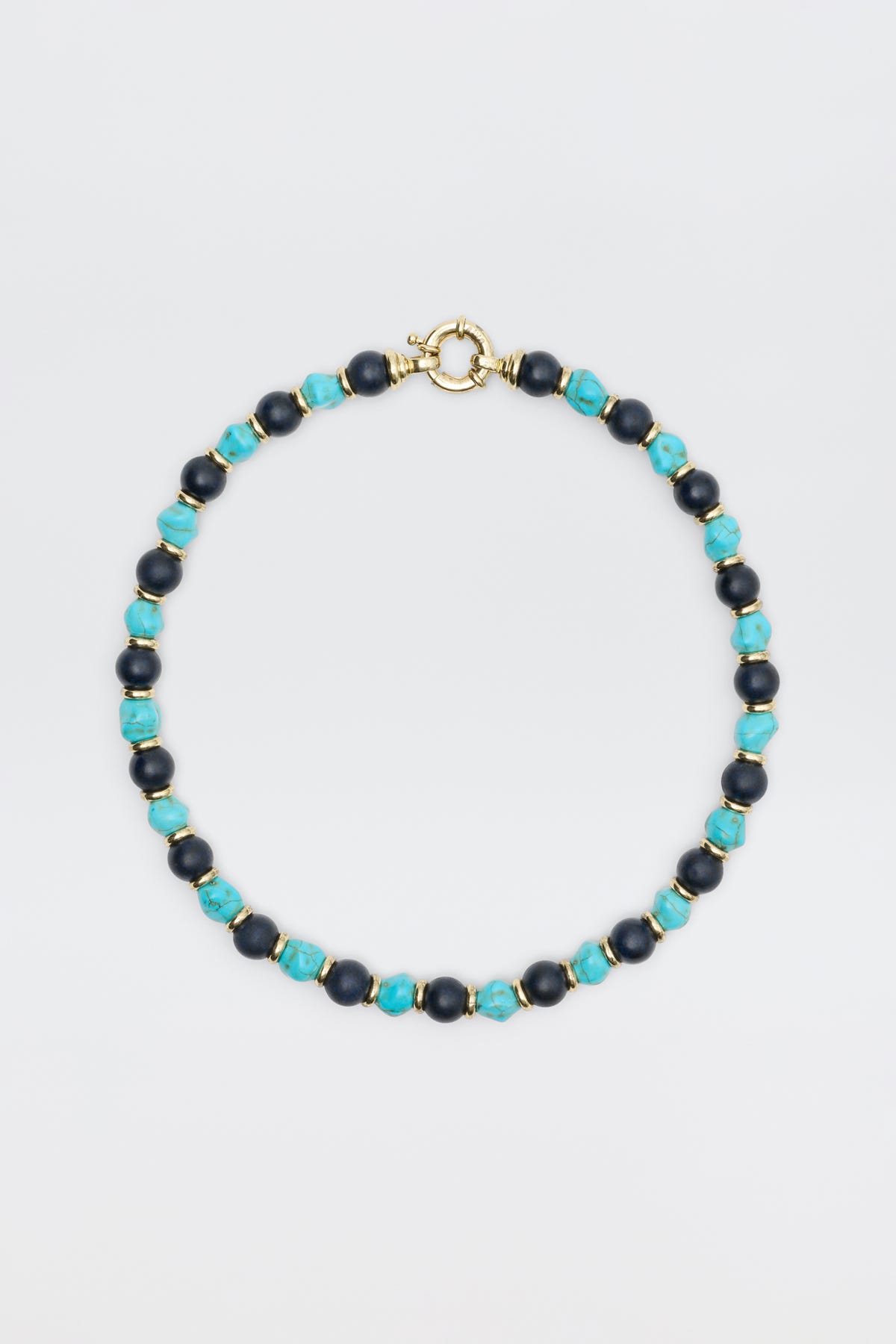 The "Palmara - Blue" necklace features alternating blue-green and dark blue round beads with gold spacers and a gold spring ring clasp, elegantly displayed against a plain light background.