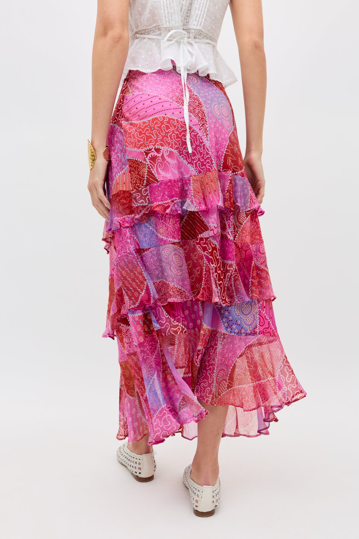 A woman is seen from the back wearing the Preslee - Ibiza Night Sunset maxi skirt in pink, red, and purple patchwork, paired with a white short-sleeved top and white perforated shoes.