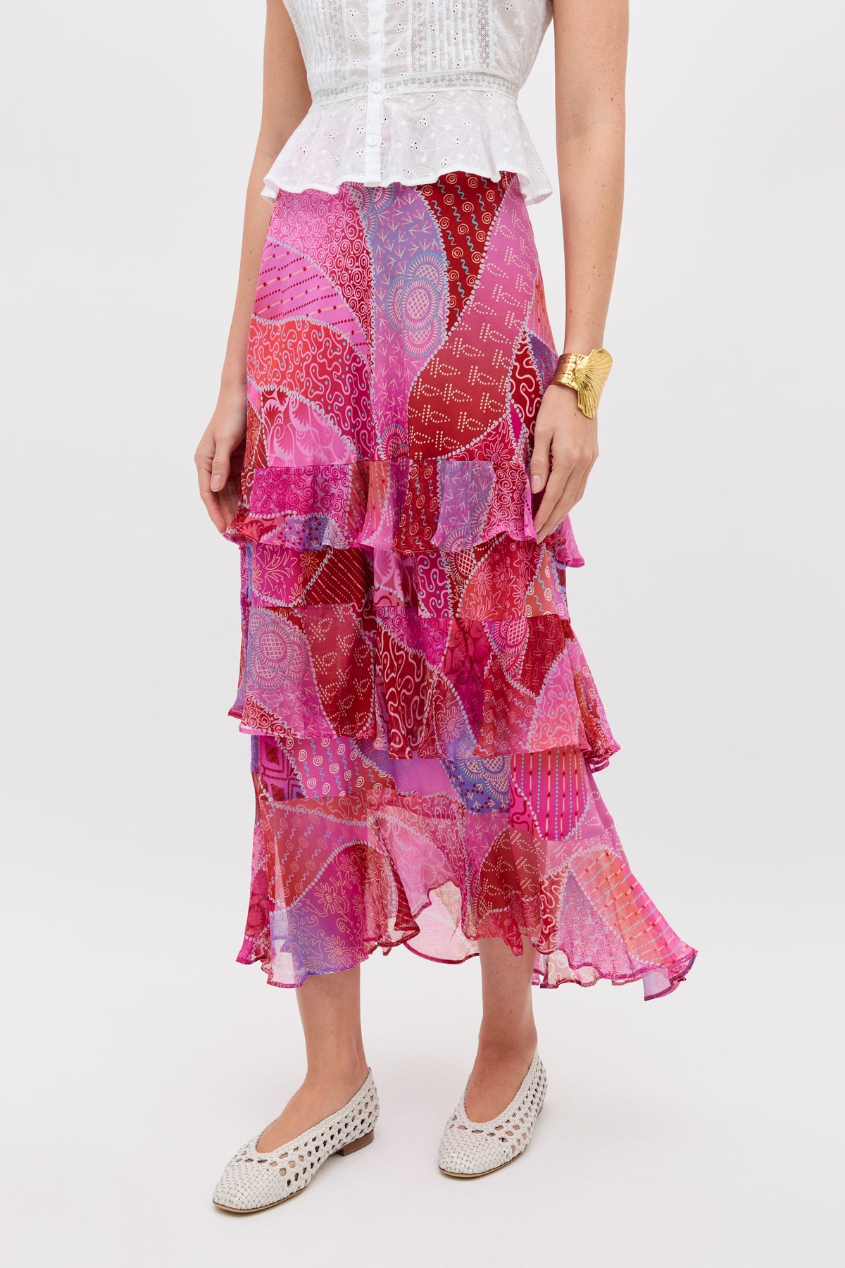 Woman wearing the Preslee - Ibiza Night Sunset, a white sleeveless blouse paired with a flowy, ruffled midi skirt in pink, red, and purple patchwork; styled with a gold bracelet and white woven flats.