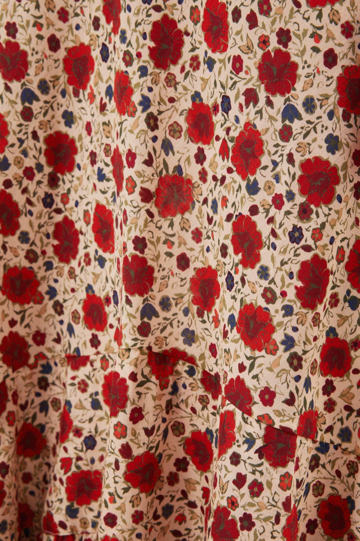Close-up of the Aenor - Eva Floral Cream fabric, a cotton-blend with red and blue flowers and green leaves on a beige background. Slight gathers highlight its texture, making it ideal for an Aenor skirt.