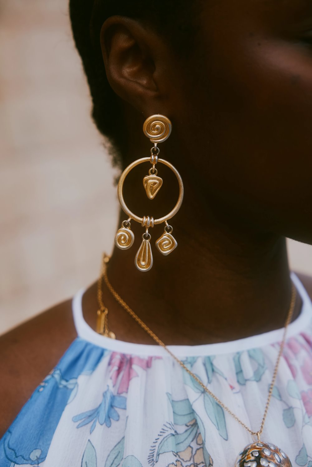 Close-up of a person wearing gold hoop earrings with dangling elements.