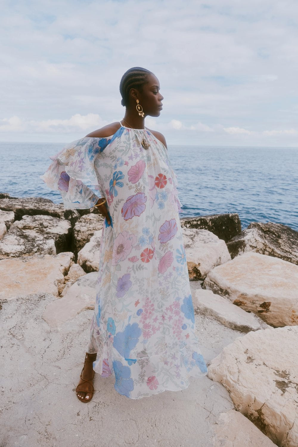 Woman in a floral dress standing on rocks by the ocean