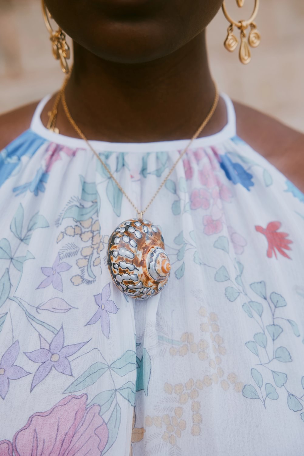 Close-up of a person wearing a floral dress and a decorative necklace with a shell pendant.