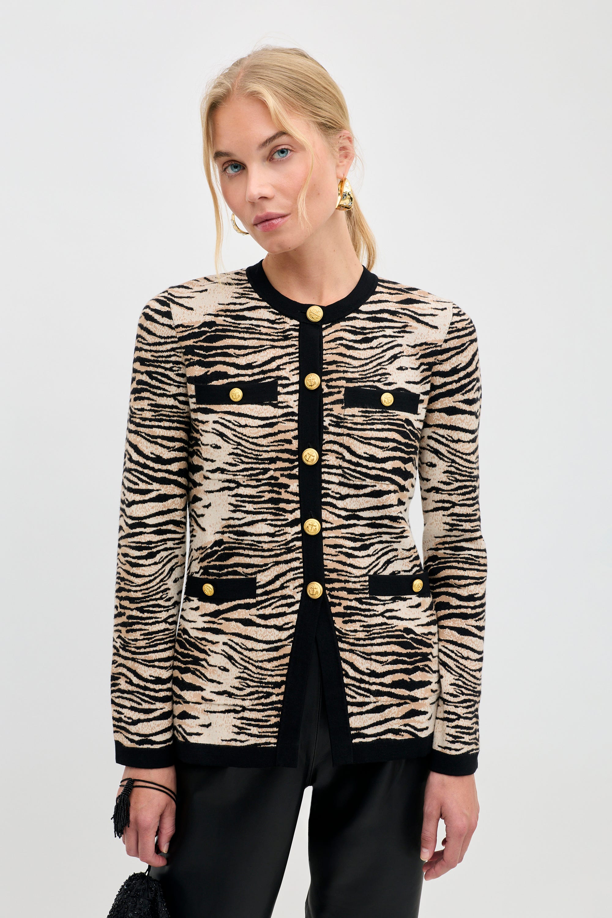 A woman wearing a Raylene - Cooper Tiger Beige cardigan in a beige and black tiger print with gold buttons.