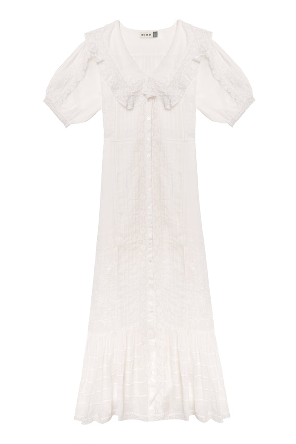 The Edina - Pansy Embroidery White dress features short sleeves, a ruffled collar, button-down front, midi length, delicate lace embroidery, flared hem, and an adjustable waist for a vintage-inspired look.