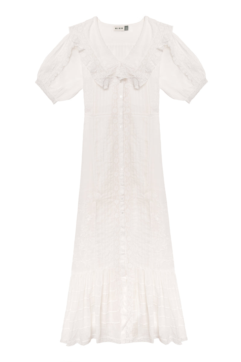 The Edina - Pansy Embroidery White dress features short sleeves, a ruffled collar, button-down front, midi length, delicate lace embroidery, flared hem, and an adjustable waist for a vintage-inspired look.