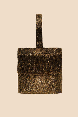 The Zenni - Beaded Gold is a small, rectangular occasion bag with a rounded top handle and gold bead fringe along the upper section, shown on a beige background.