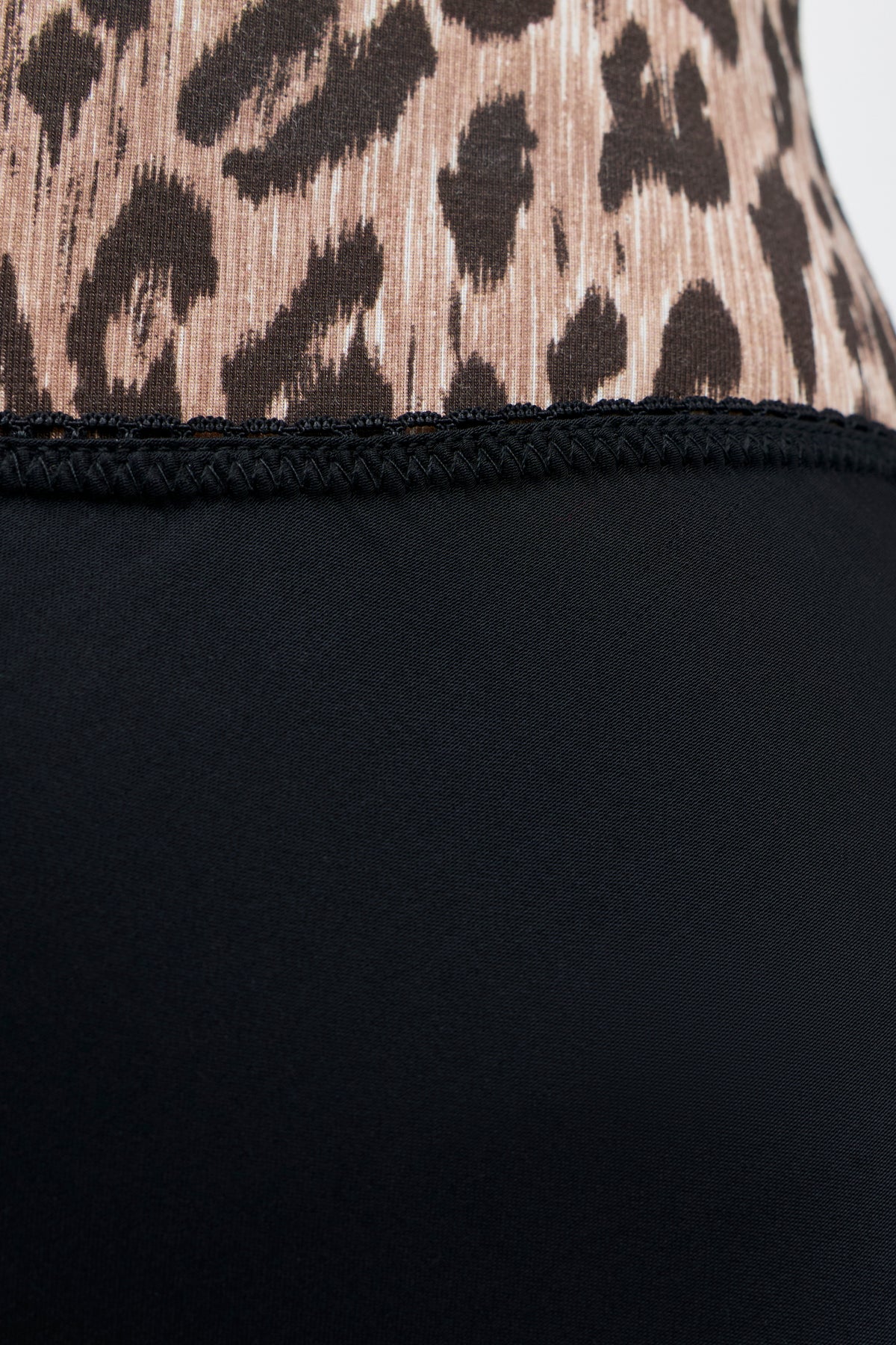 Close-up of the Stassie - Black fabric, featuring a tan and black leopard print pattern on top and a solid black matte satin skirt fabric below, separated by a row of black stitching.