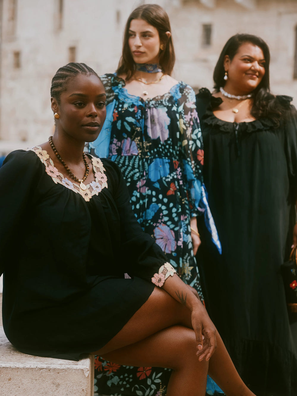 Three women in dresses standing outdoors with a building in the background