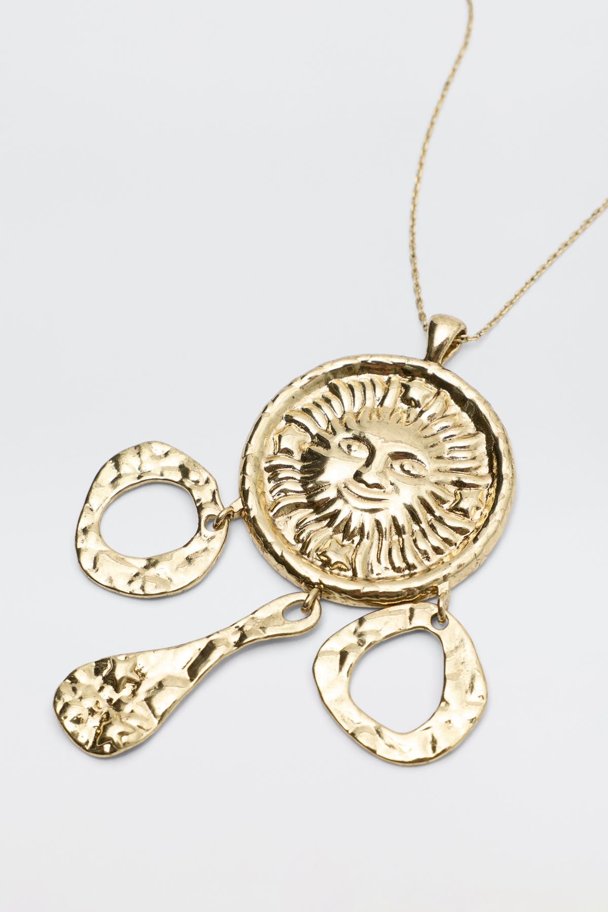 The Zahra - Gold necklace features a round sun face medallion pendant with three hammered gold dangles hanging below.