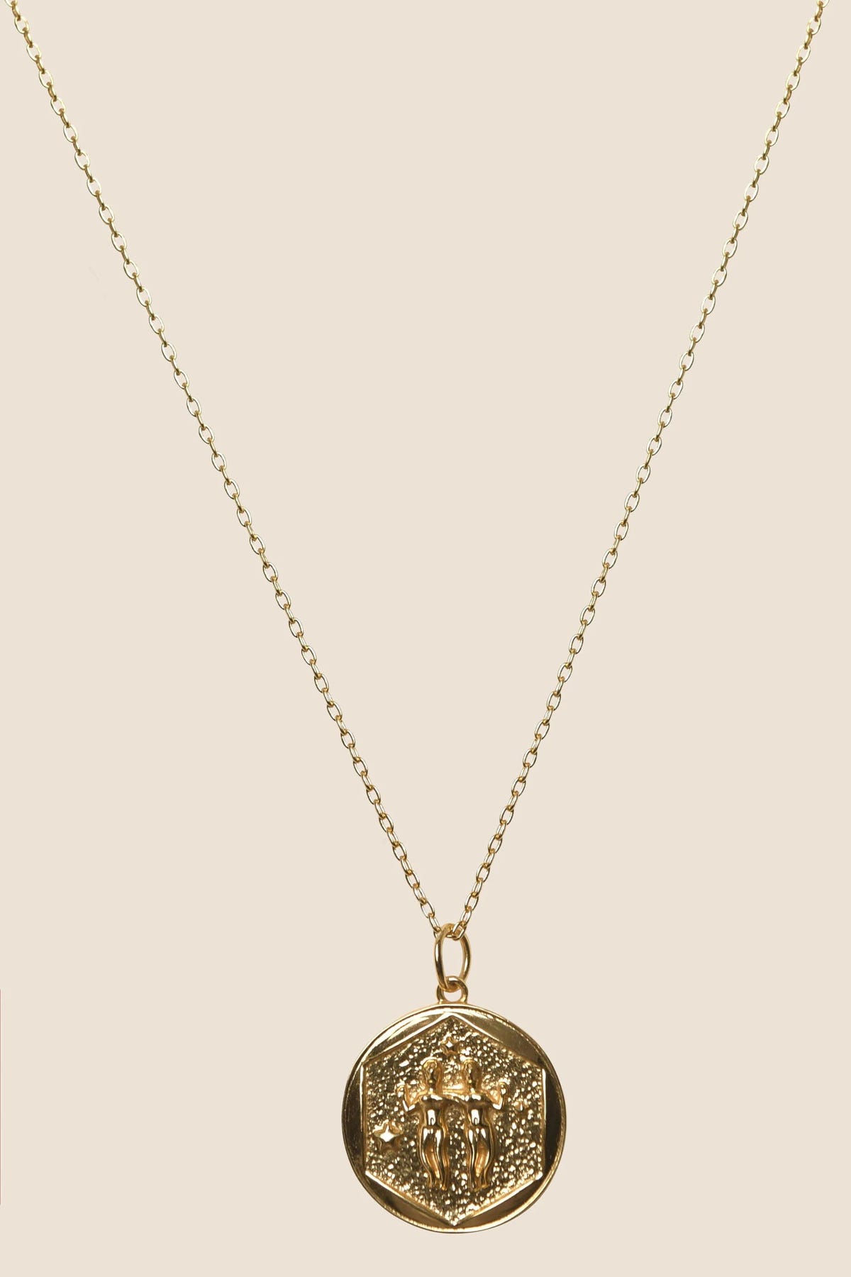 The Zodiac - Gemini gold vermeil necklace features a fine chain and an embossed oval pendant, shown on a beige background—ideal for those looking for an elegant Gemini zodiac necklace.