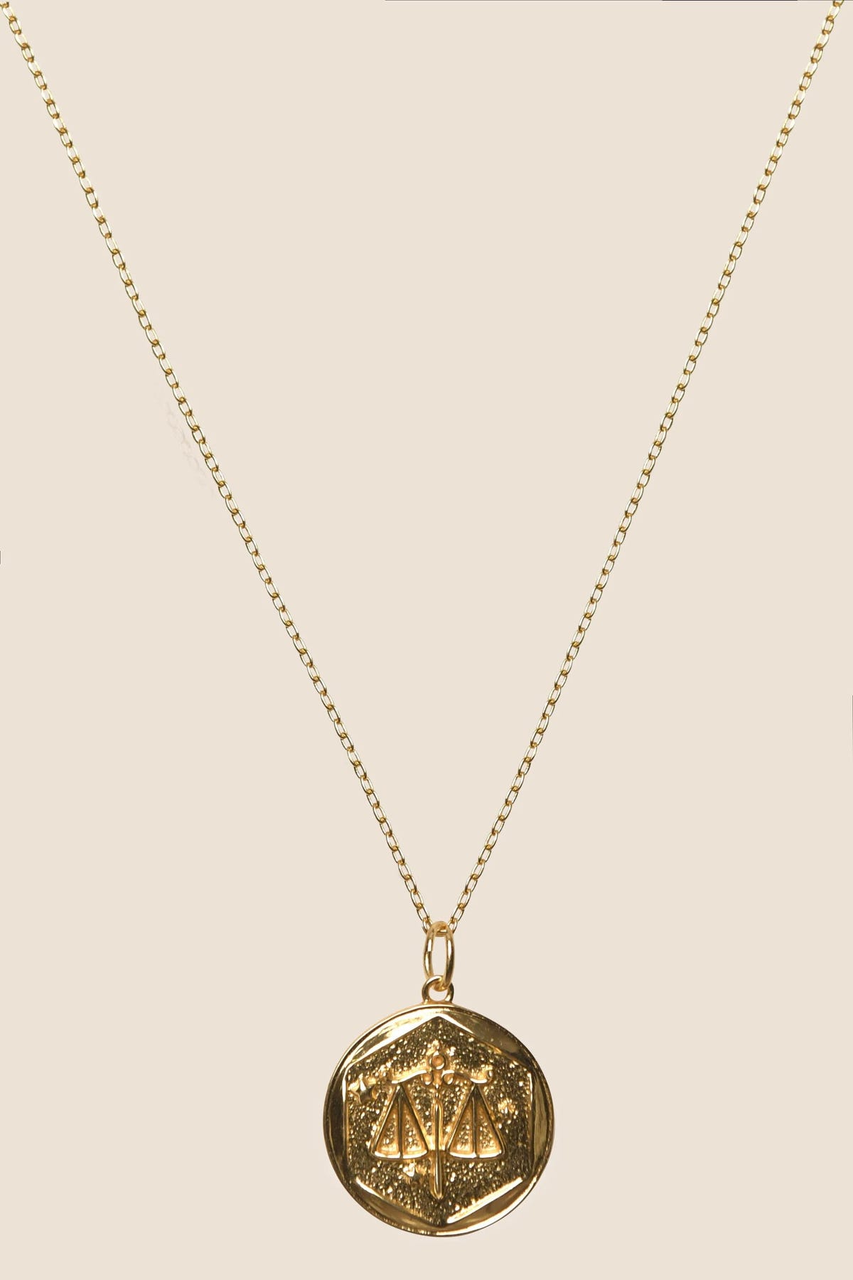 Zodiac - Libra: A gold vermeil chain necklace with a round, engraved pendant featuring geometric designs and star-like patterns, reminiscent of modern Zodiac necklaces, displayed against a plain, light background.