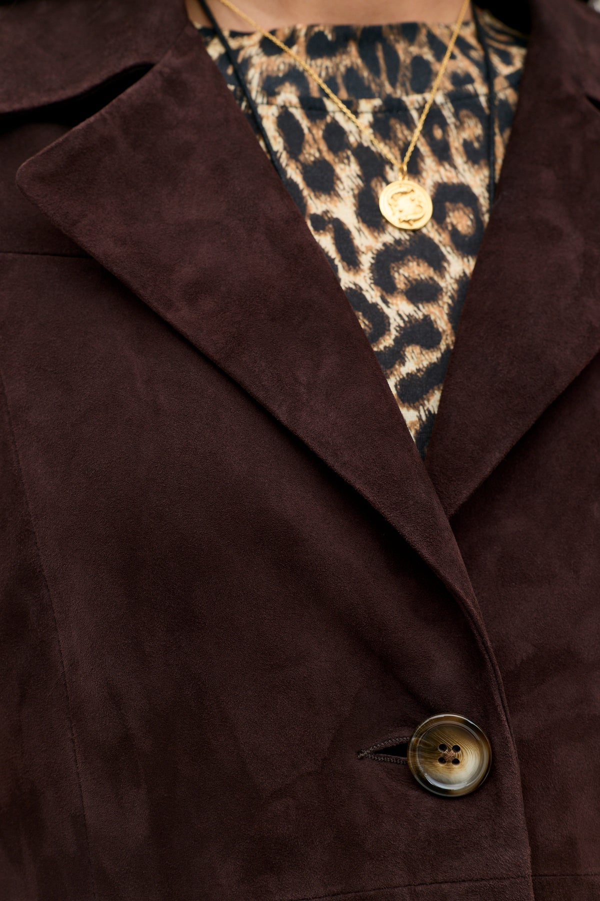 Close-up of the Astraea - Chocolate vintage suede coat in rich brown, featuring a single button, worn over a leopard print top and accessorized with two gold necklaces.