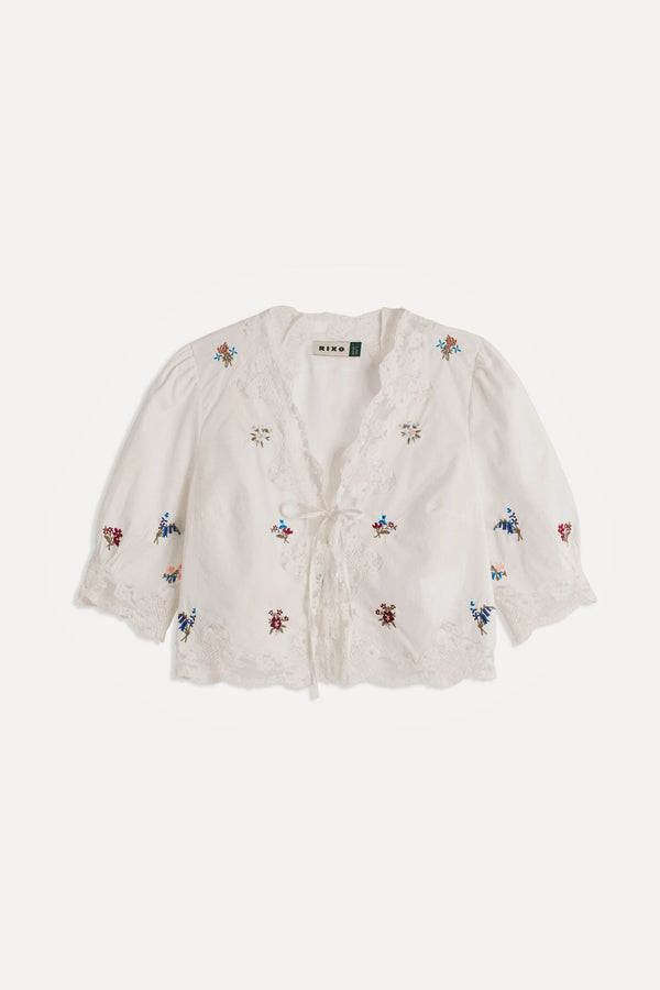 The Ursula - Bud Embroidery White top is a white, short-sleeved style with lace trim, a tie front, and small colorful floral embroidery for effortless vintage charm.
