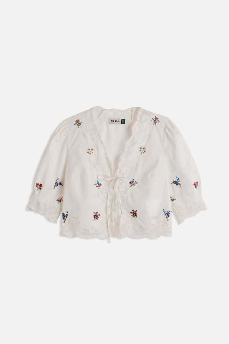 The Ursula - Bud Embroidery White top is a white, short-sleeved style with lace trim, a tie front, and small colorful floral embroidery for effortless vintage charm.