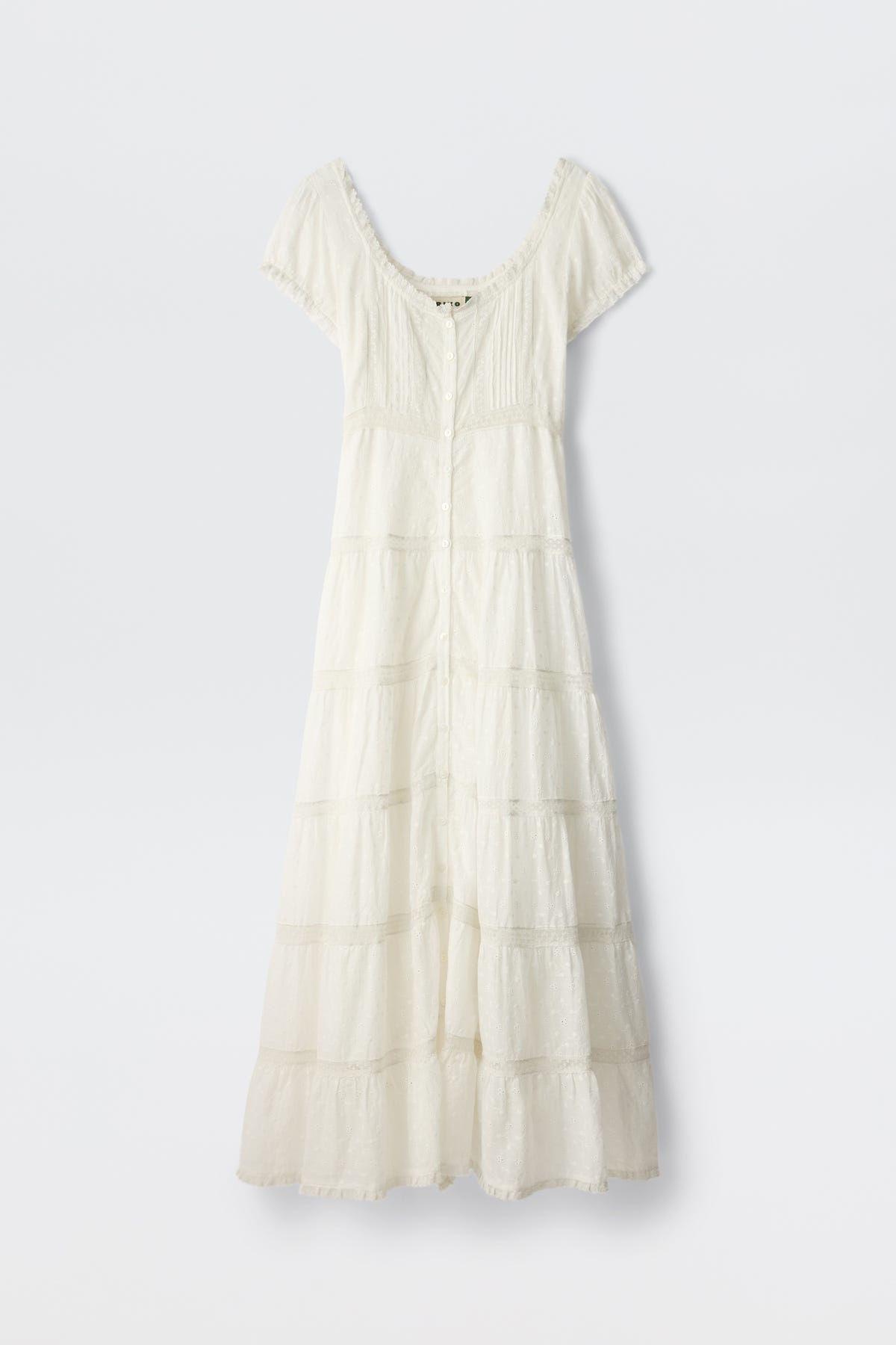 The Jaclyn - Ivory is a white cotton summer dress with short sleeves, an ankle-length tiered skirt, fitted bodice, button-down front, and lace-trimmed neckline and sleeves. The delicate fabric has a textured broderie anglaise pattern.