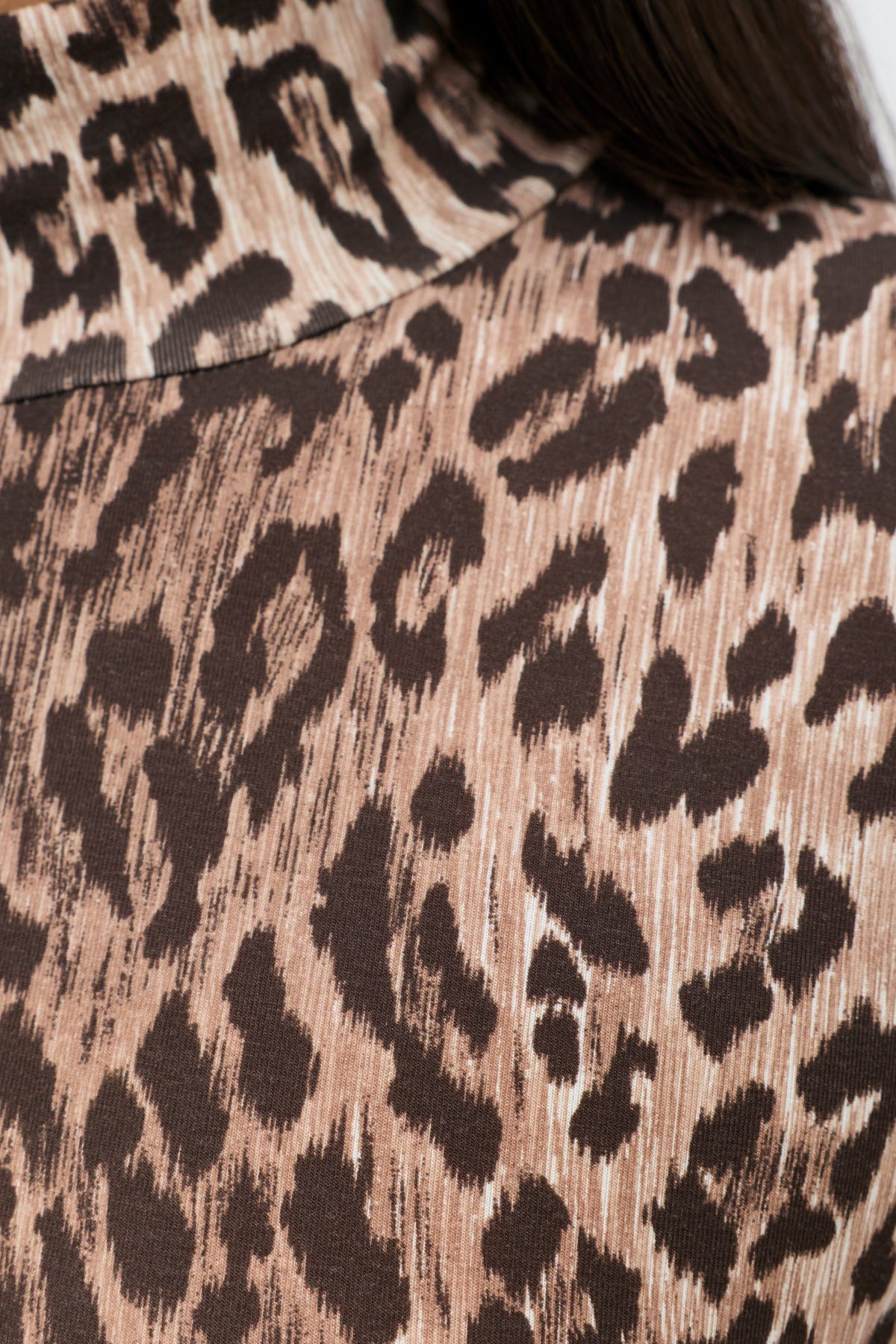 Close-up of a person wearing the Polo - Leopard Brown, a turtleneck top featuring a detailed brown and black leopard print made from soft TENCEL™ Modal fabric. Part of dark hair is visible at the top right.