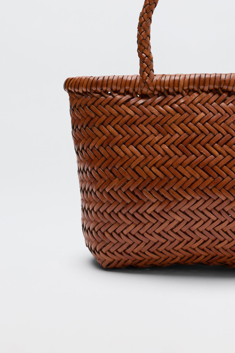 Close-up of the Lysia - Tan basket with a braided handle, showcasing its detailed herringbone pattern in a warm brown hue against a plain white background. Reminiscent of vintage woven bags, this piece combines timeless style with modern craftsmanship.