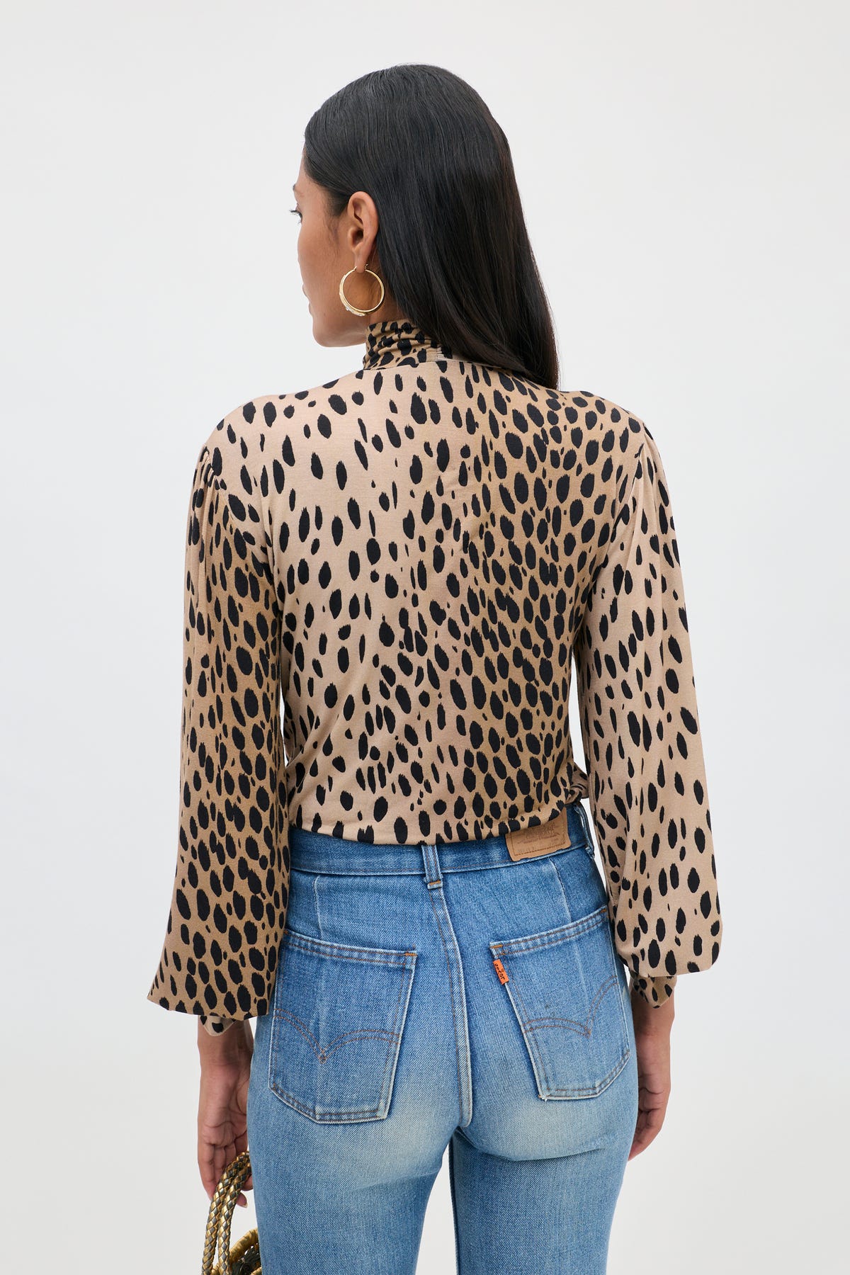 A person with long dark hair wears the Suki - Antelope Spot Black top and blue jeans, standing with their back to the camera against a plain light background.