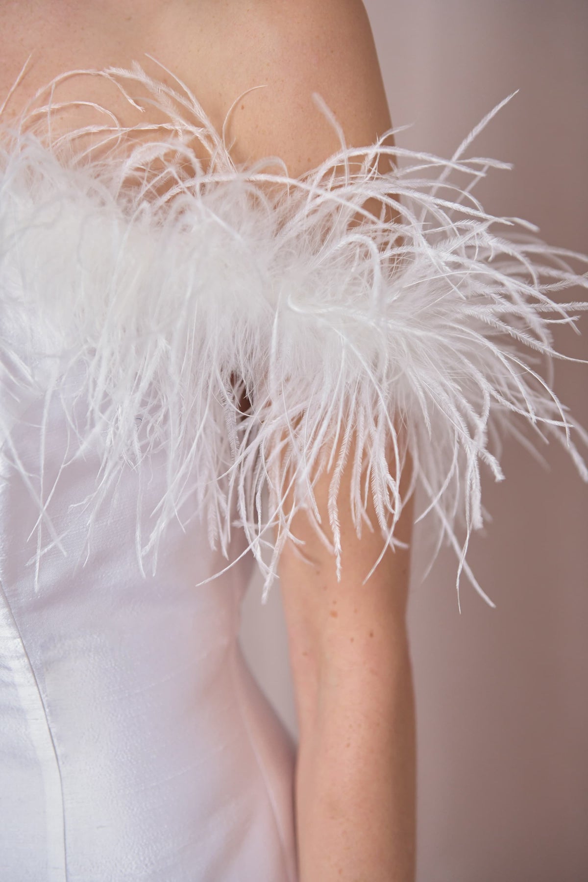Close-up of a person wearing the Lena - Feather Ivory dress, featuring an off-the-shoulder Bardot neckline with feather trim and a luxurious ivory satin finish, shown against a soft neutral background.